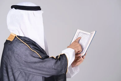 رجل إماراتي بالزي التقليدي يقرأ القرآن الكريم