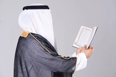 رجل إماراتي يمسك بالقرآن الكريم بالبشت التقليدي