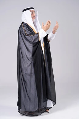 رجل إماراتي يرتدي البشت ويدعو على خلفية رمادية