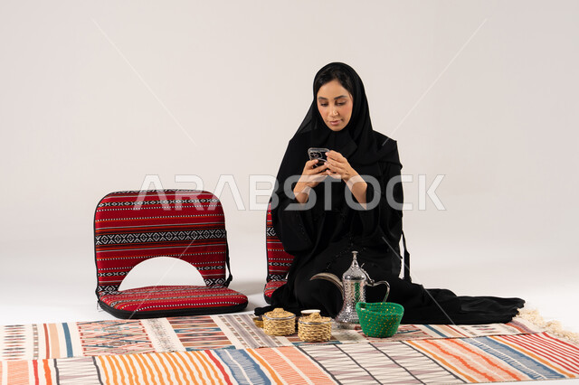 امرأة سعودية مع هاتف ذكي ودلة قهوة تقليدية