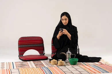 امرأة سعودية مع هاتف ذكي ودلة قهوة تقليدية