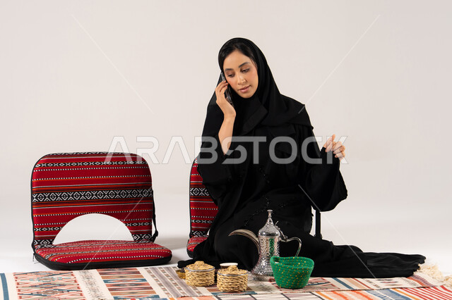 امرأة سعودية بالعباءة تتحدث بالهاتف مع دلة قهوة