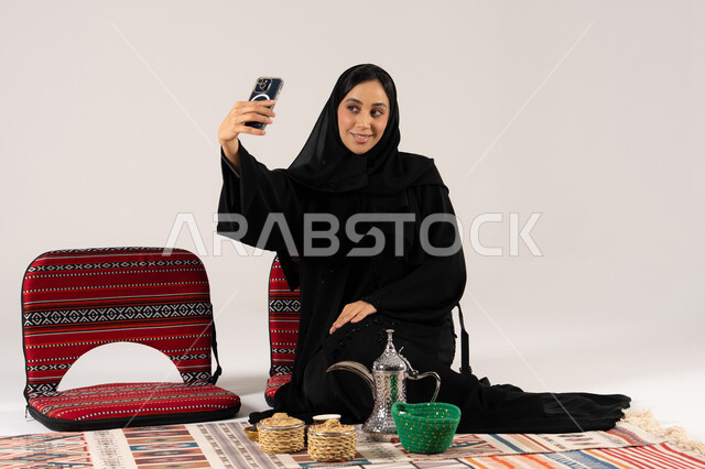امرأة سعودية بالعباءة تلتقط سيلفي مع دلة القهوة