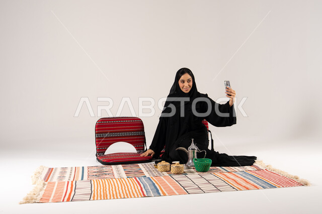 امرأة سعودية بالعباءة تلتقط سيلفي مع ديكور شعبي