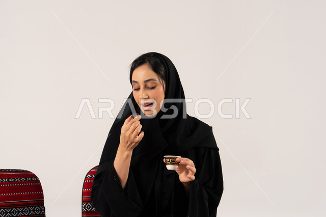 امرأة سعودية بالعباءة تتناول التمر والقهوة