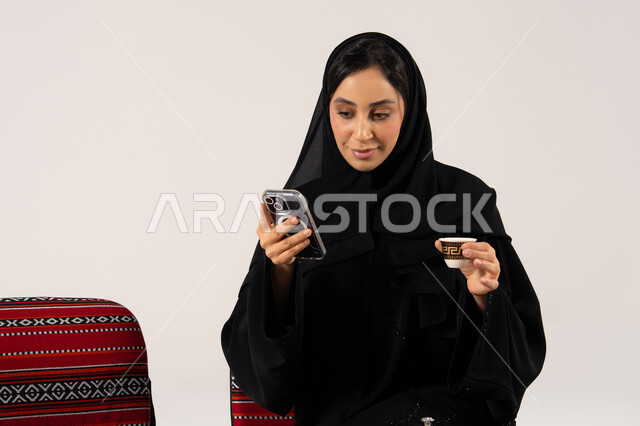 امرأة سعودية تستخدم الجوال مع فنجان قهوة عربية