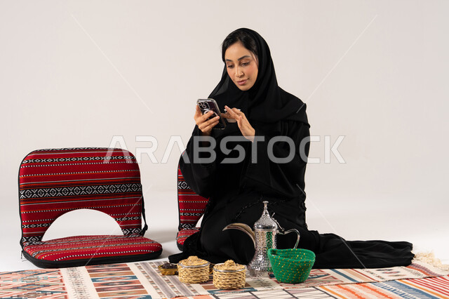 امرأة سعودية تستخدم الجوال مع أدوات القهوة التراثية