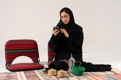 امرأة سعودية تستخدم الجوال مع أدوات القهوة التراثية