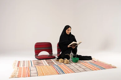 امرأة سعودية تقرأ كتاباً على سجادة تراثية في استوديو