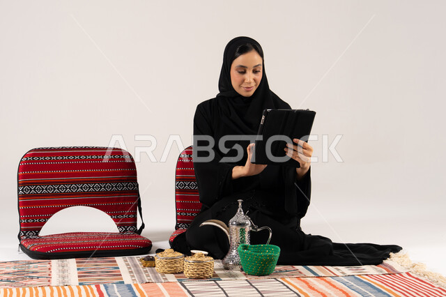 امرأة سعودية تستخدم جهاز لوحي مع طقم قهوة عربية