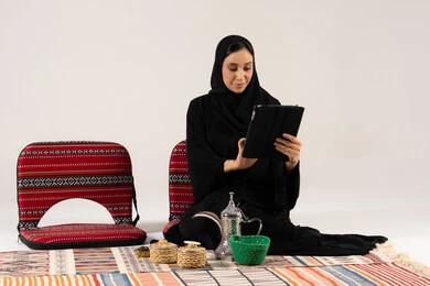 Saudi Woman Using Tablet with Traditional Arabic Coffee Set