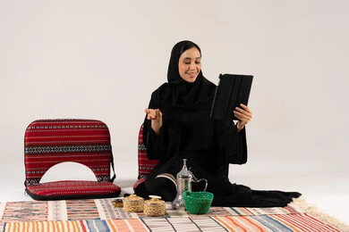 Saudi Woman Using Tablet on Traditional Sadu Floor Seat Saudi Woman Using Tablet on Traditional Sadu Floor Seat