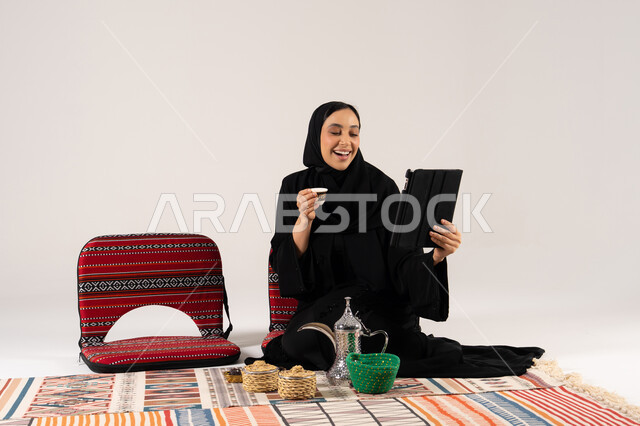 امرأة سعودية بالعباءة تستخدم جهاز لوحي وتشرب القهوة
