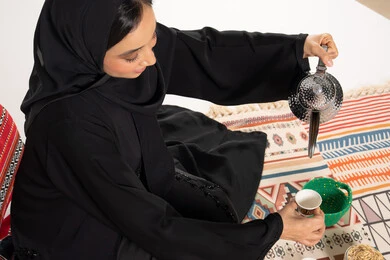 امرأة سعودية تصب القهوة العربية بالعباءة التقليدية