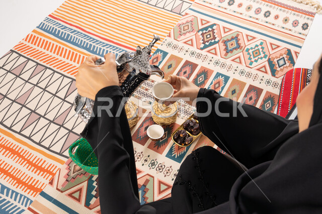 امرأة بالعباءة تصب القهوة العربية على سجادة سدو