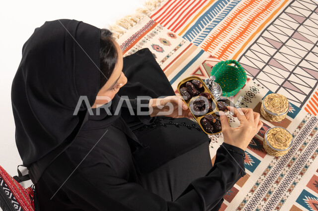 امرأة عربية بالعباءة تتناول التمر على سجادة تقليدية