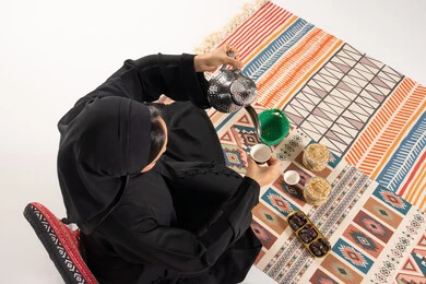 امرأة إماراتية تسكب القهوة العربية على سجادة تقليدية