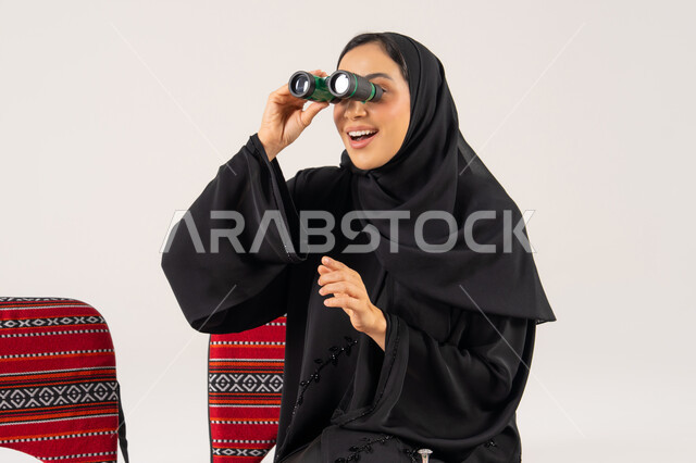 امرأة عربية بالعباءة تستخدم المنظار في استوديو تصوير