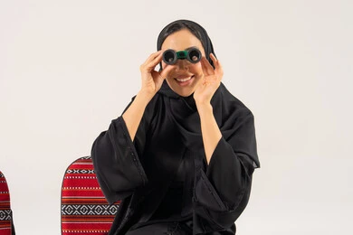 امرأة سعودية تحمل منظار مكبر على كرسي سدو