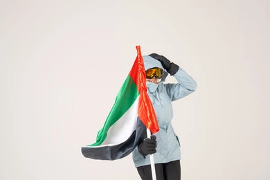 شخص يحمل علم الإمارات بملابس التزلج الشتوية