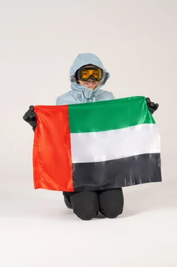 رجل بملابس التزلج يحمل علم الإمارات على خلفية بيضاء