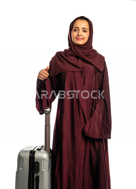 بورتريه إمرأة سائحة عربية خليجية سعودية تمسك حقيبة السفر ، ترتدي العباءة الخليجية ، سياحة وفندقة ، قضاء أوقات ممتعة في الإجازة ، سياحة وسفر ، الإستعداد للرحلة السياحية ، رحلة عمل , خلفية بيضاء .