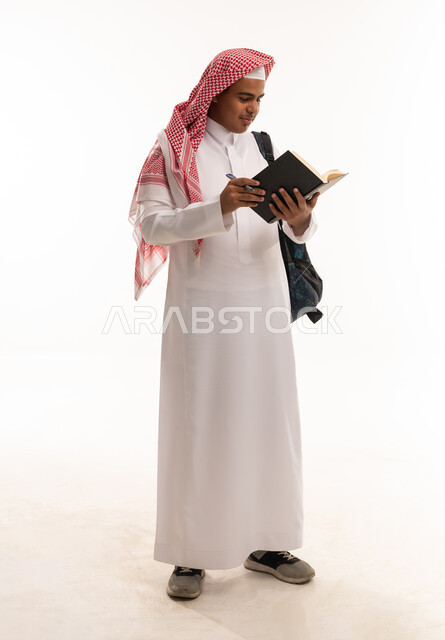 طالب سعودي يرتدي الثوب التقليدي يقرأ كتاباً على خلفية بيضاء