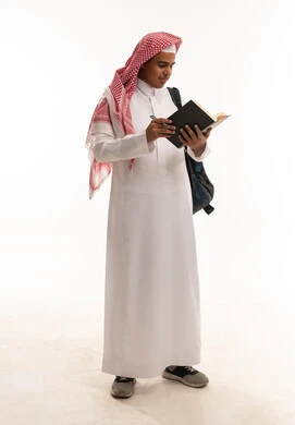 طالب سعودي يرتدي الثوب التقليدي يقرأ كتاباً على خلفية بيضاء