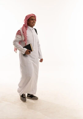 رجل سعودي بالزي التقليدي يمشي حاملاً كتاباً