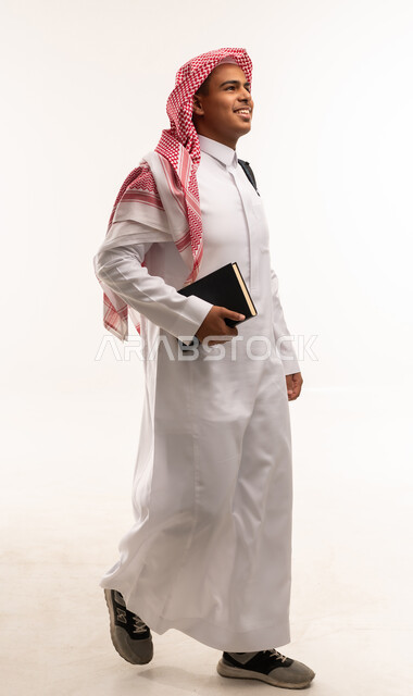 رجل سعودي بالزي التقليدي يمشي حاملاً كتاباً