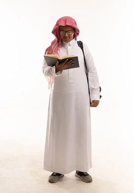 طالب سعودي يرتدي الزي التقليدي يقرأ كتاباً