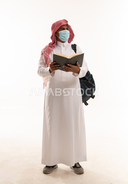 طالب سعودي بالثوب والكمامة يحمل كتاباً خلفية بيضاء