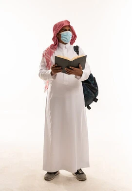طالب سعودي بالثوب والكمامة يحمل كتاباً خلفية بيضاء