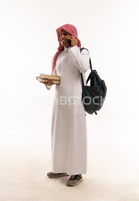 طالب سعودي يحمل كتباً وهاتفاً ذكياً في الاستوديو