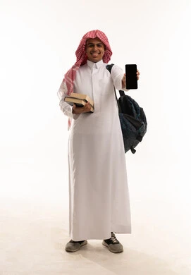 طالب سعودي بالثوب التقليدي يحمل هاتفاً ذكياً وكتباً