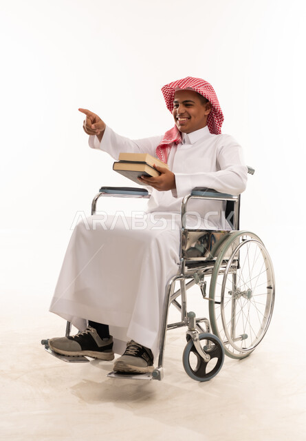 رجل سعودي على كرسي متحرك يحمل كتباً ويشير للأمام