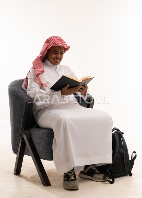 طالب سعودي يقرأ كتاباً على كرسي مع حقيبة ظهر