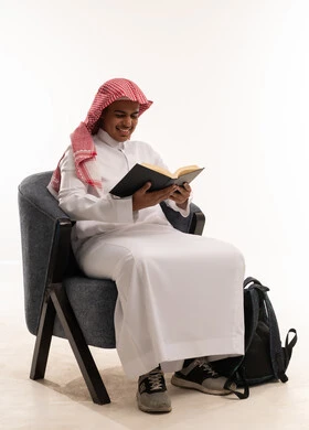 طالب سعودي يقرأ كتاباً على كرسي مع حقيبة ظهر
