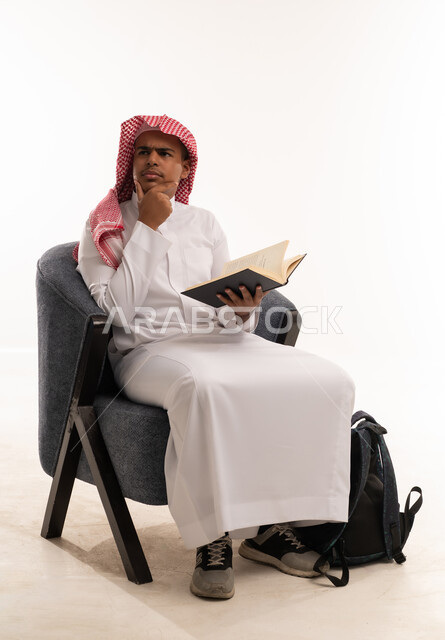 طالب سعودي يرتدي الثوب التقليدي يقرأ كتاباً في استوديو