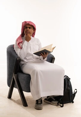 طالب سعودي يرتدي الثوب التقليدي يقرأ كتاباً في استوديو