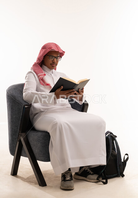 طالب سعودي يرتدي الثوب التقليدي يقرأ كتاباً في الاستوديو