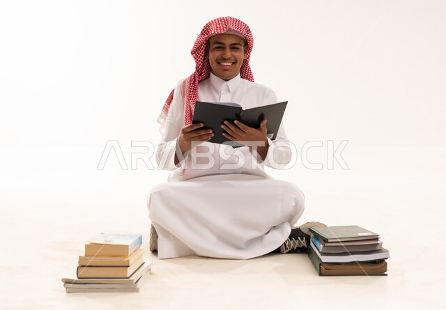 شاب سعودي بالزي التقليدي يقرأ كتاباً في الاستوديو