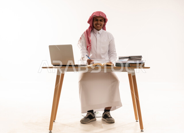 رجل سعودي على مكتب مع لابتوب وكتب خلفية بيضاء