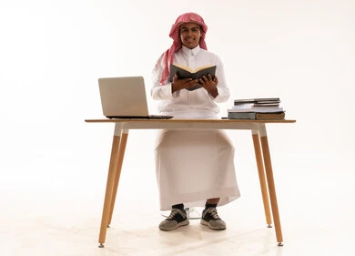 Saudi Man in Traditional Thobe Reading at Desk