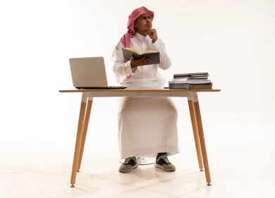 رجل سعودي يفكر خلف المكتب مع لابتوب وكتب