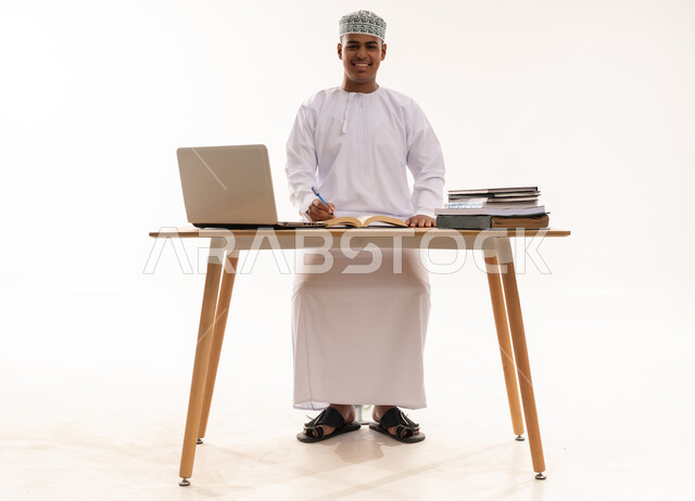 رجل عماني خلف مكتب مع حاسوب محمول وكتب
