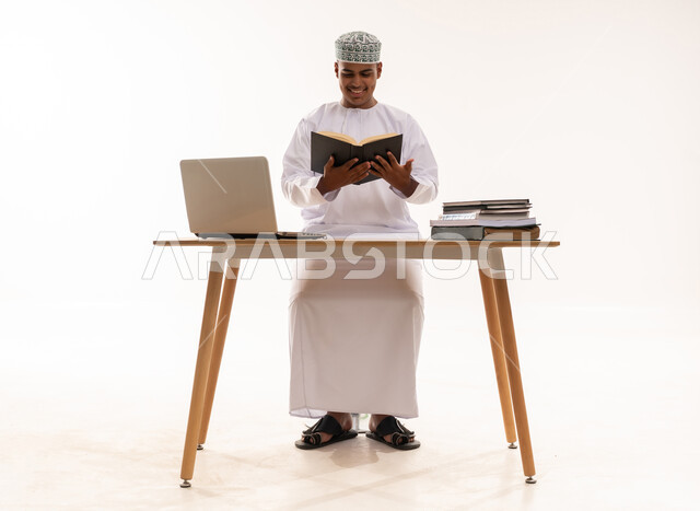 رجل عماني يقرأ كتاباً على مكتب مع لابتوب