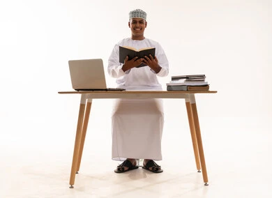 رجل عُماني يدرس مع جهاز حاسوب وكتب خلفية بيضاء رجل عُماني يدرس مع جهاز حاسوب وكتب خلفية بيضاء