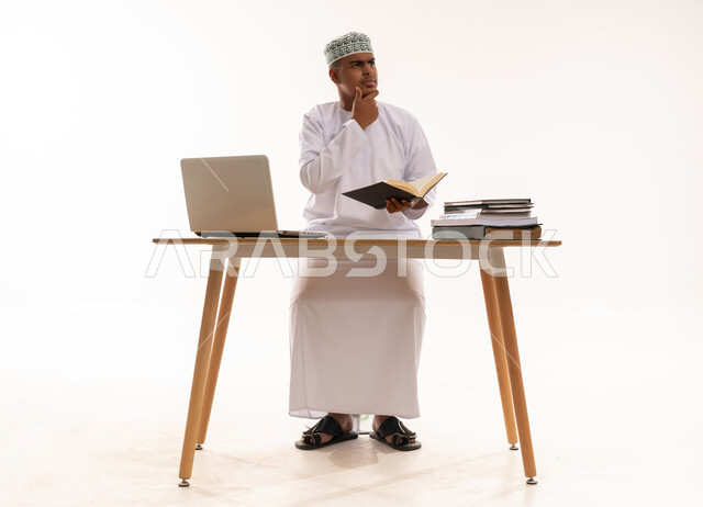 رجل عماني يجلس خلف مكتب مع لابتوب وكتب