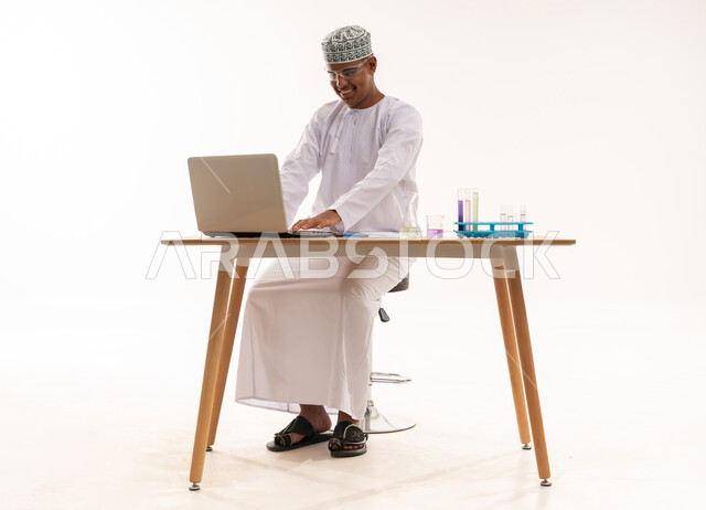 رجل عماني يعمل على حاسوب مع أدوات مختبرية